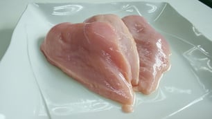 Raw chicken breast fillets on a white plate.